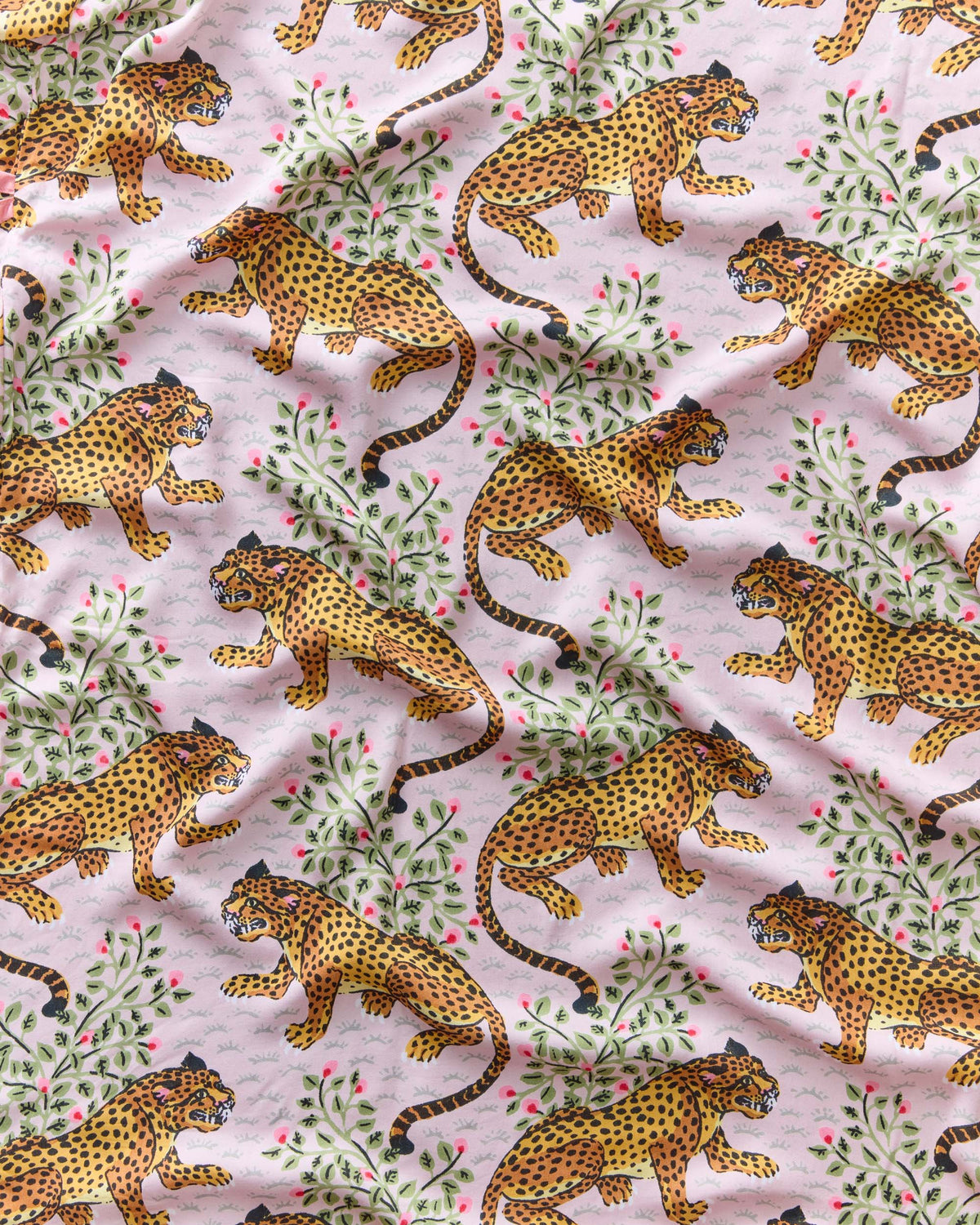 Blush fabric swatch with repeating illustrated leopards among leafy branches and pink flowers.