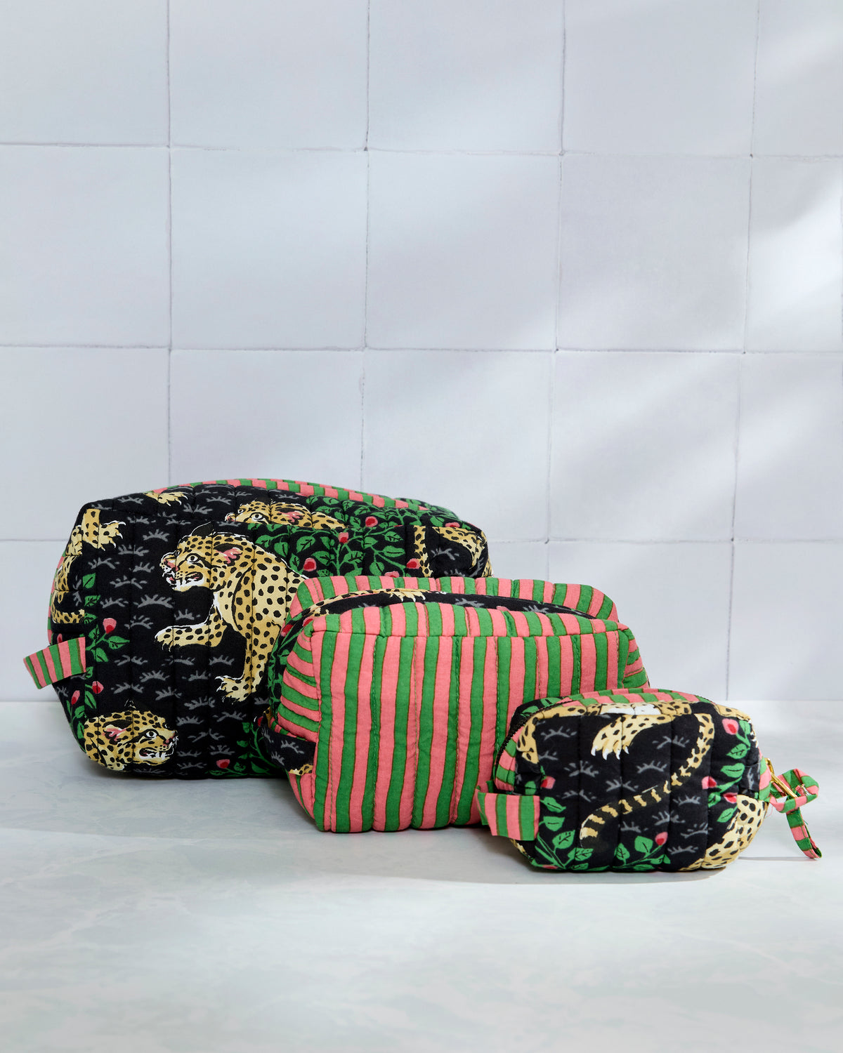 Three quilted pouches arranged by size, with leopard print on the largest and smallest pouches and pink-and-green stripes on the middle pouch.
