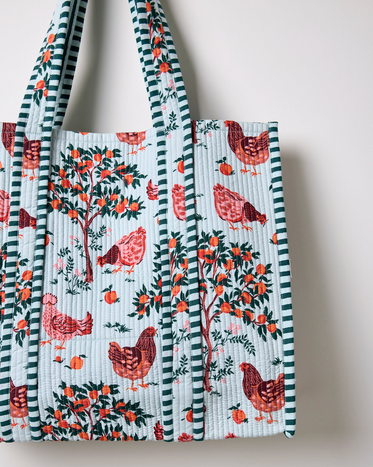 Close-up of the quilted tote bag showing its light blue farmyard print, vertical quilting, and striped trim.