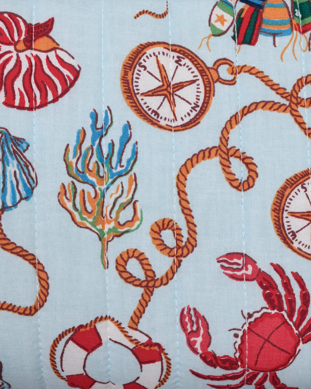 Close-up of a light blue nautical pattern with compasses, rope loops, seashells, coral, and a red crab.