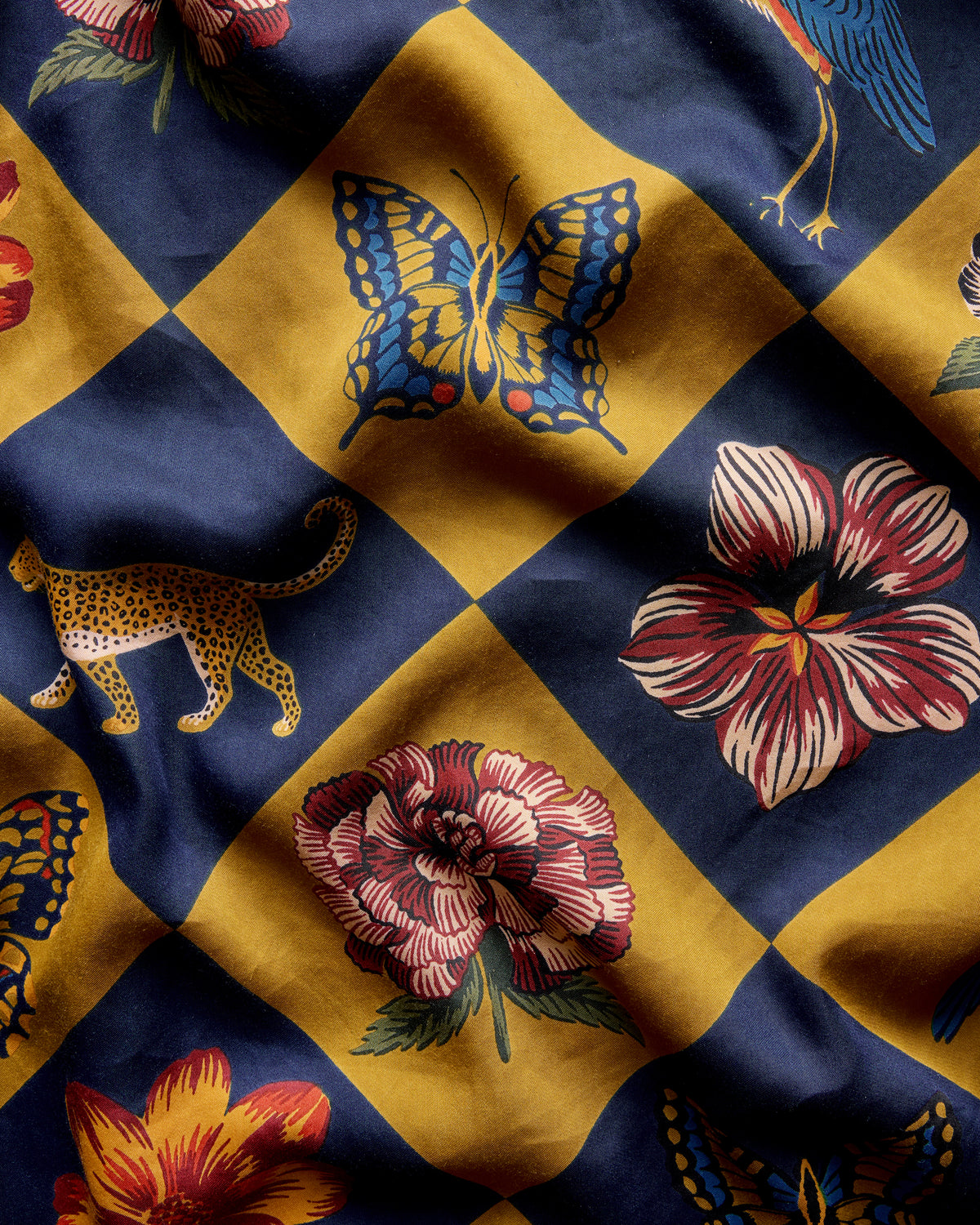 Close-up of Botanical Checkerboard fabric with navy and golden diamond blocks featuring butterflies, birds, leopards, and flowers.