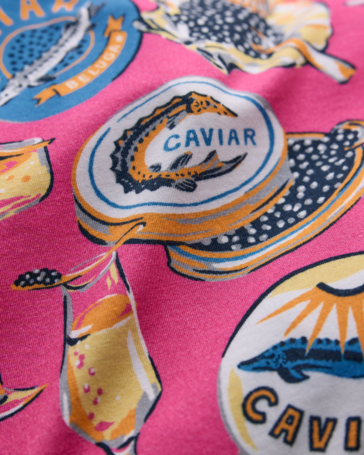 Close-up of the Champagne & Caviar print showing a caviar tin, champagne glass, and fish illustrations on hot pink fabric.