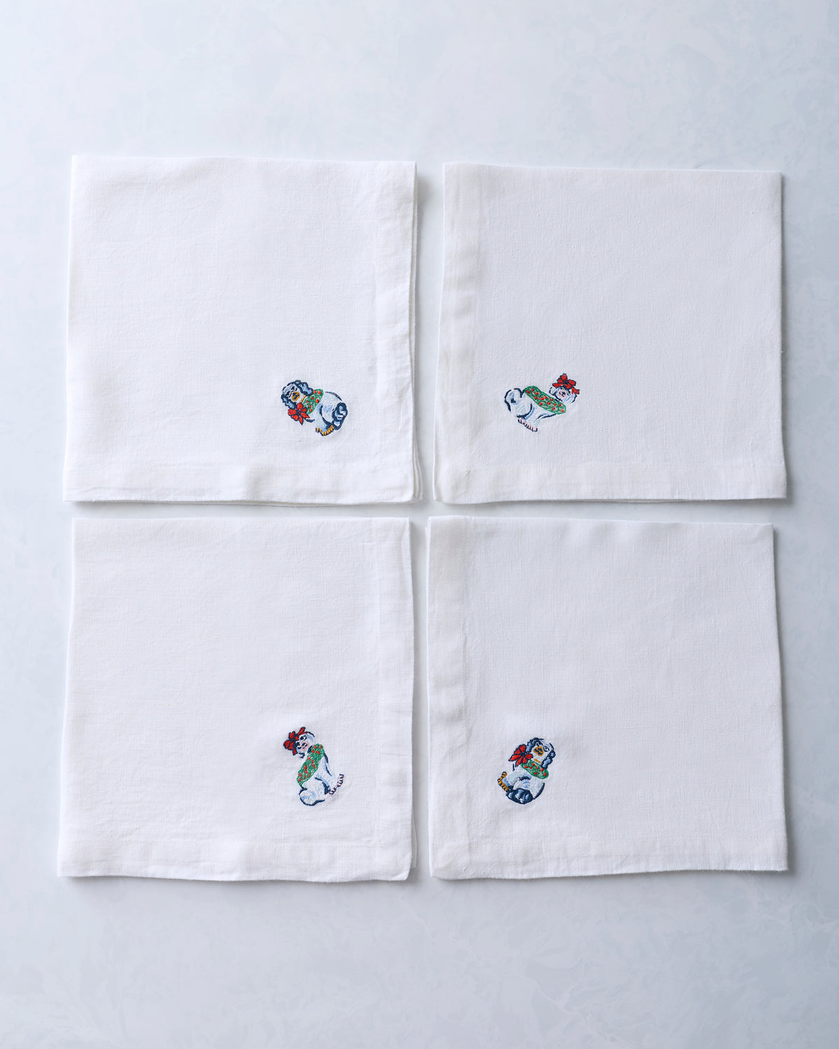 Set of four white dinner napkins arranged in a square, each with an embroidered dog figurine