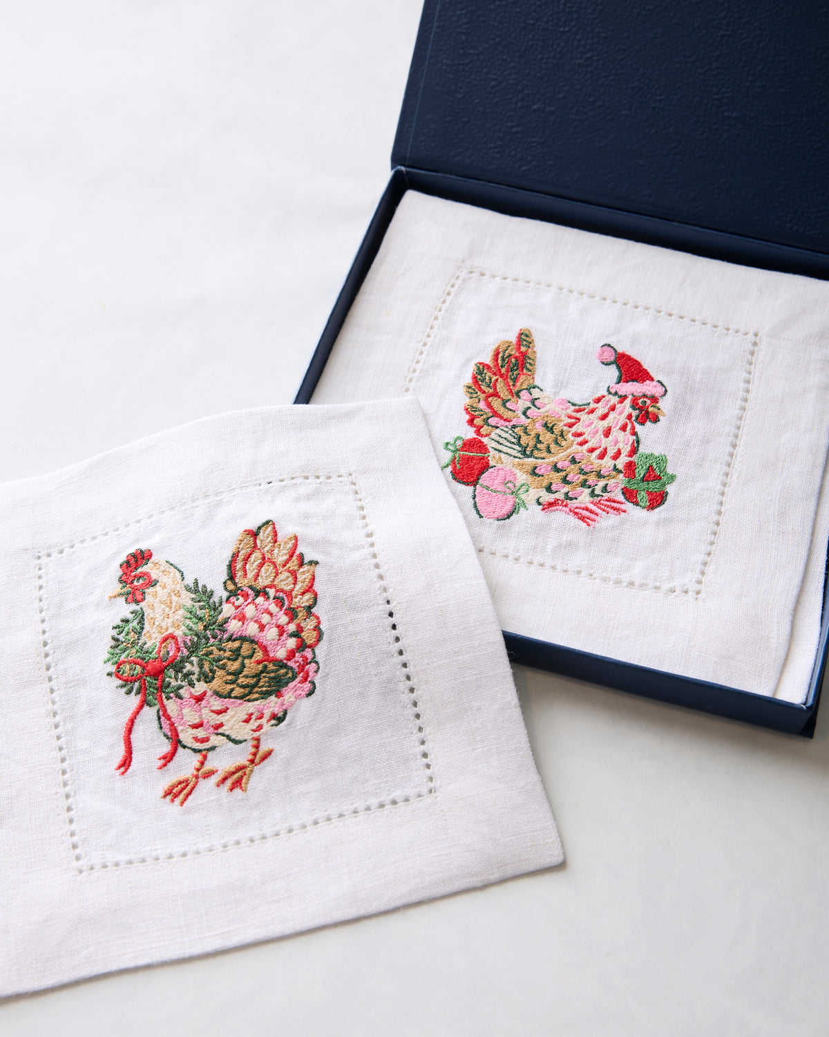 Two embroidered chicken cocktail napkins displayed, one inside an open dark box