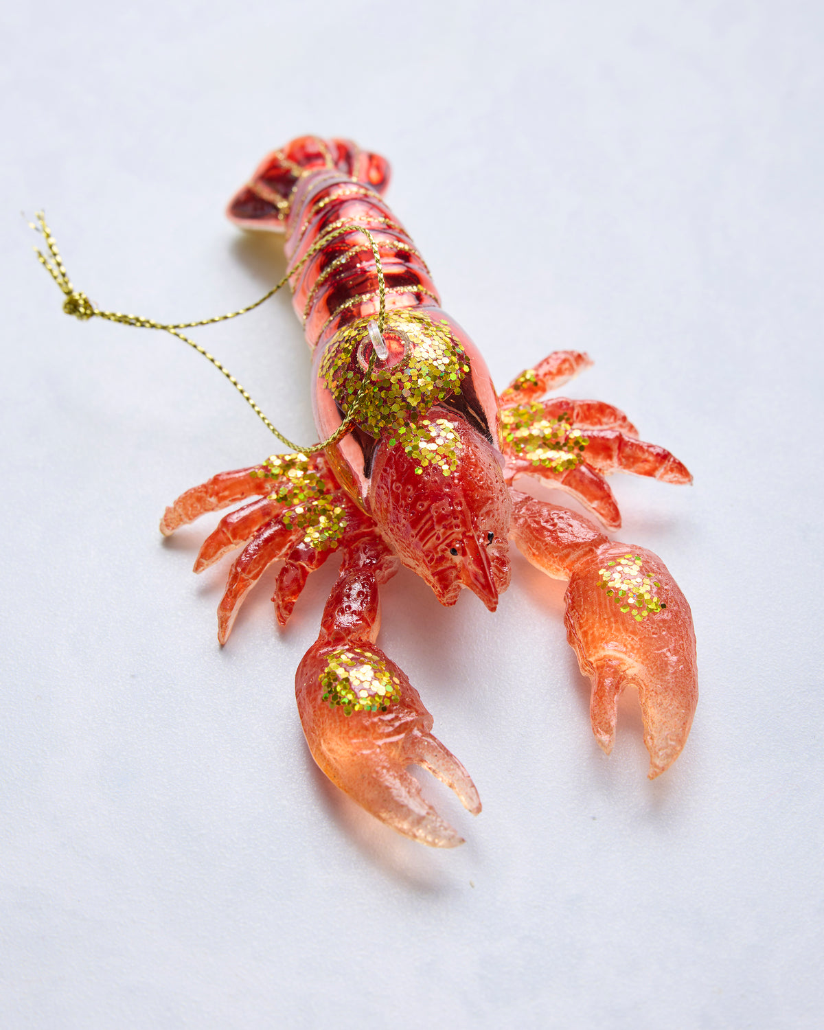 Close angled view of a red lobster glass ornament with glittered claws, body, and hanging loop.