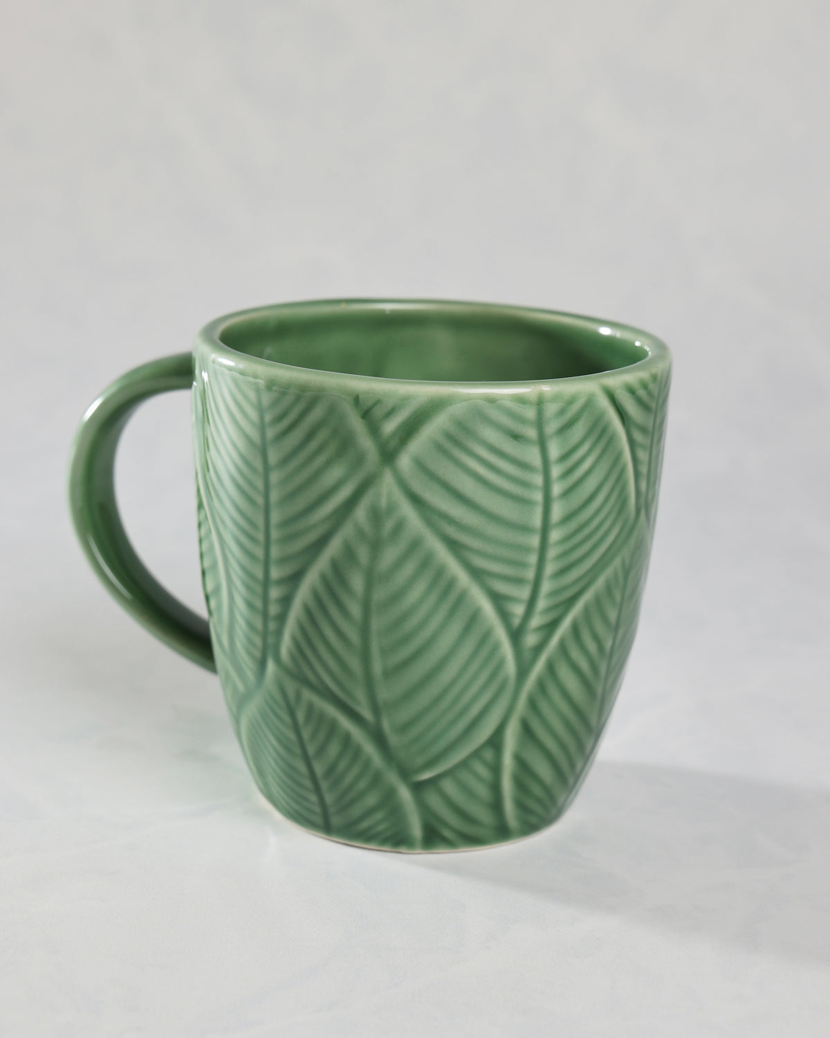 Green leaf-patterned mug shown from the back with an empty interior and handle on the left.