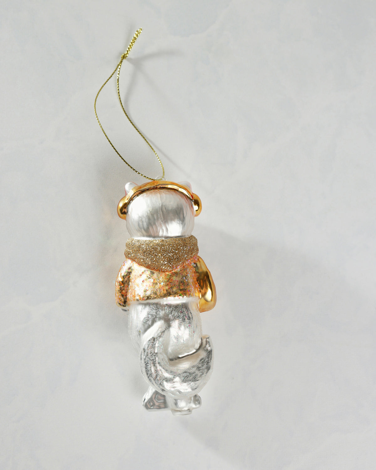 Back view of the silver-and-gold cat ornament showing its hanging cord, glittered clothing, and curled lower body.