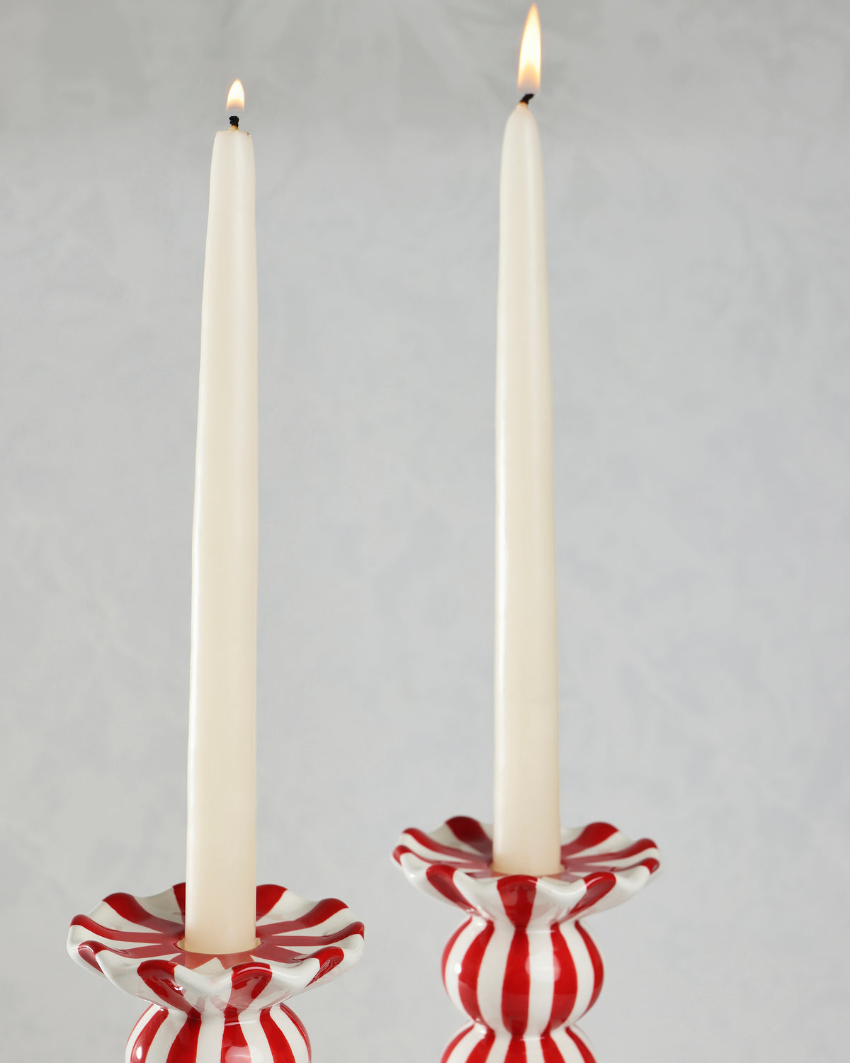 Two red-and-white striped ruffle candle holders with tall white candles lit.