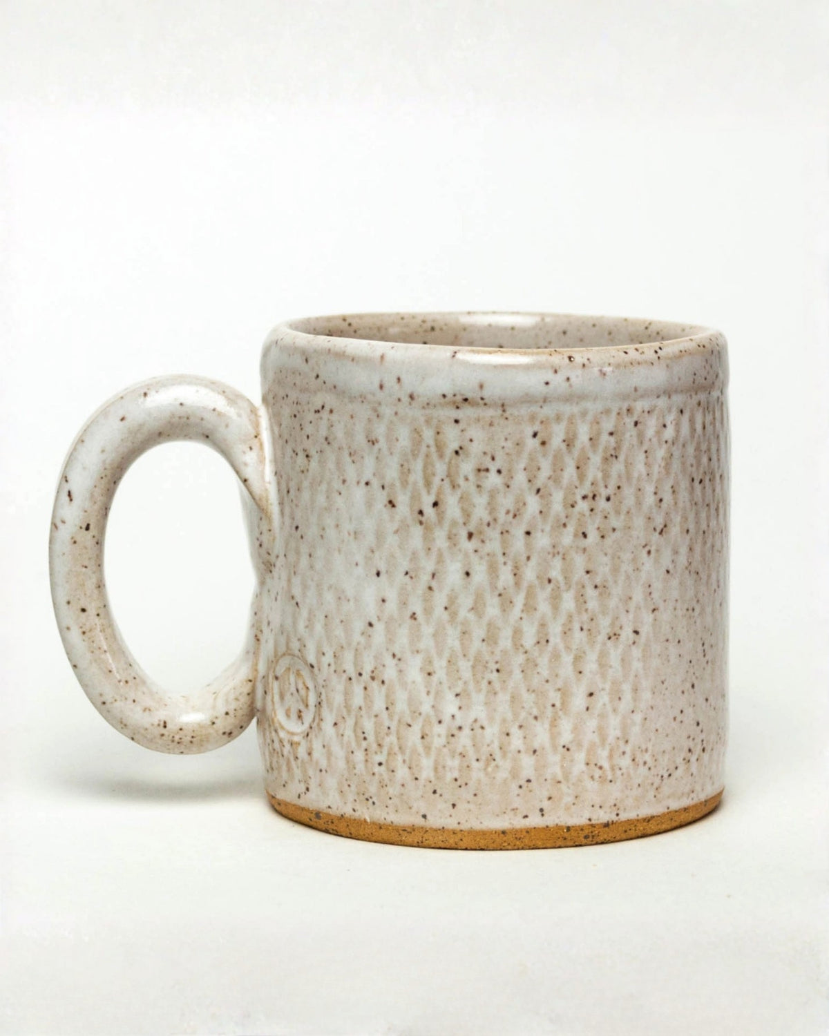Back of an ivory speckled ceramic mug with a handle on the left and a small circular mark near the base.