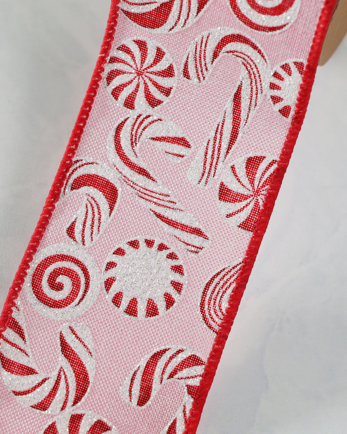 Close-up of pink wired peppermint ribbon showing red-and-white candy shapes and glitter details.