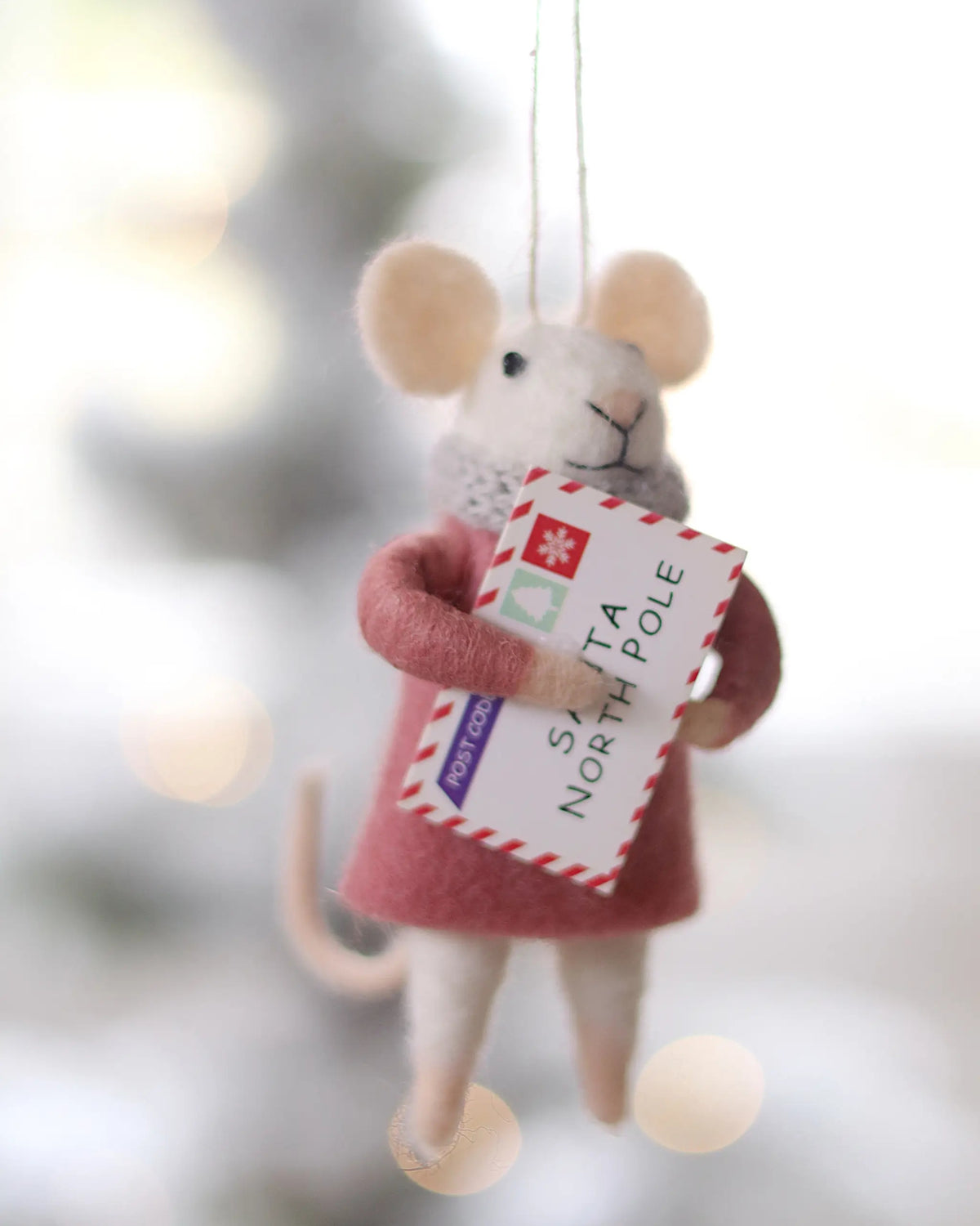 Felt mouse ornament holding a Santa North Pole envelope, shown hanging against a softly blurred background.