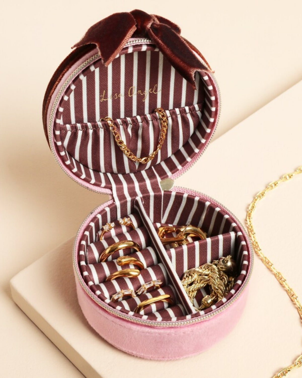 Open pink round jewelry case showing striped lining, ring rolls, compartments, and jewelry storage.