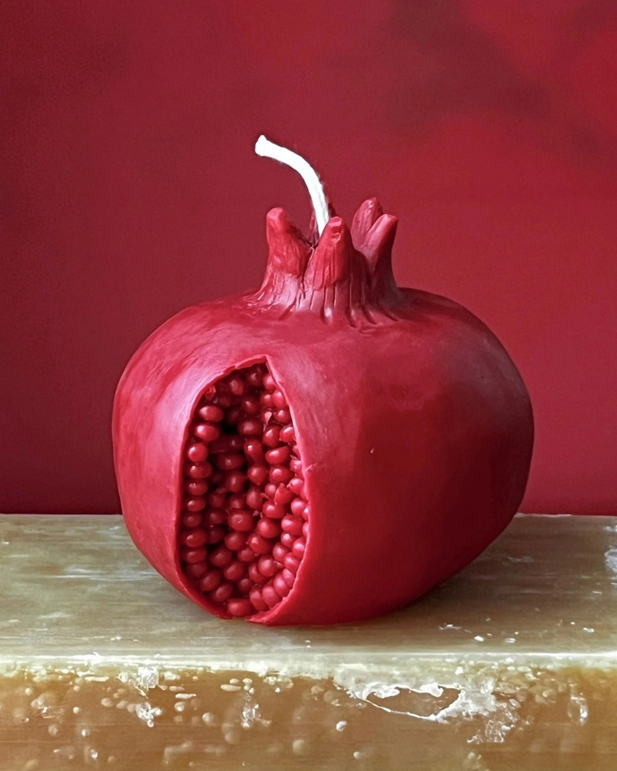Red pomegranate-shaped beeswax candle with a white wick on a wooden surface.