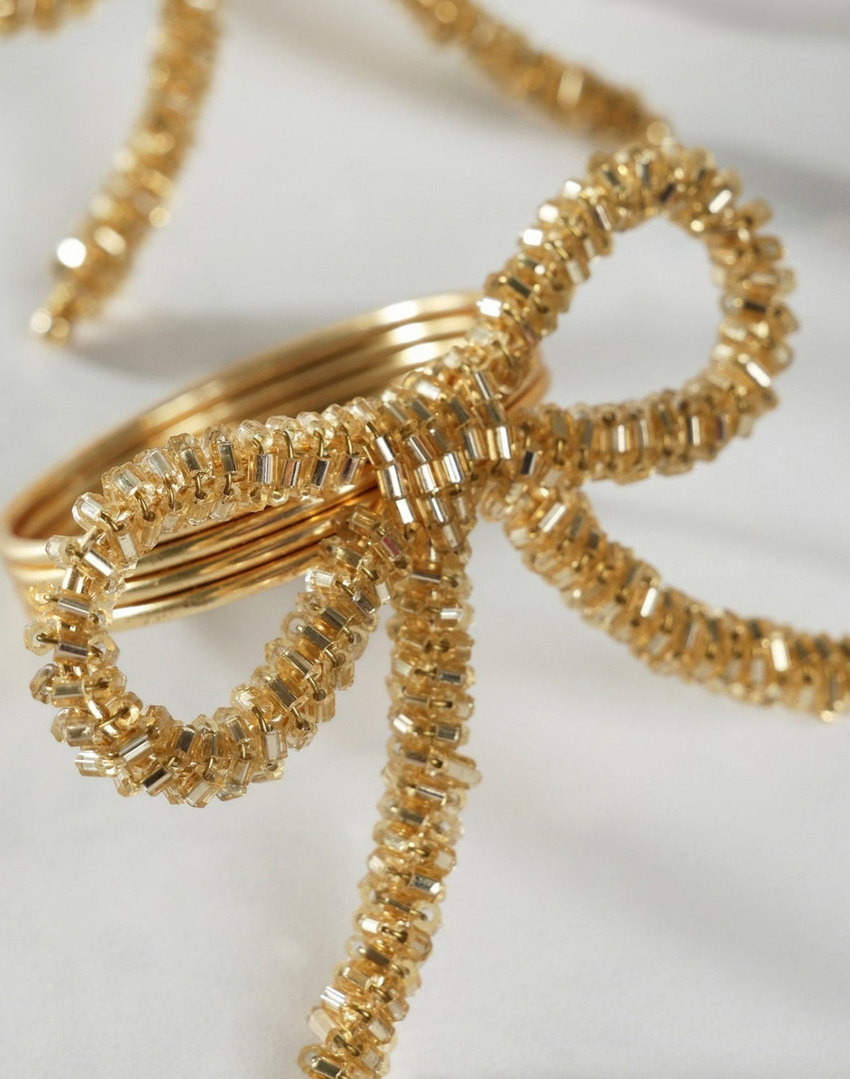 Close-up of two gold bow napkin rings with beaded detailing and trailing bow tails.