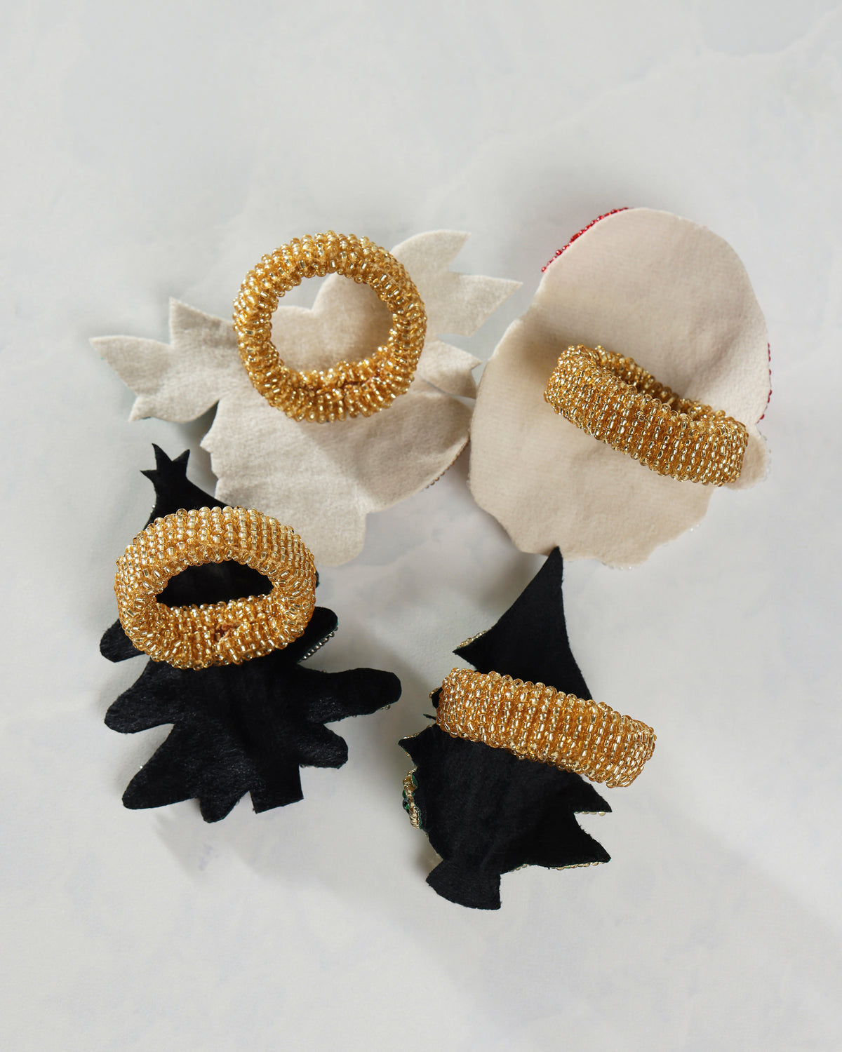Four gold Santa napkin rings arranged on black and white fabric shapes.