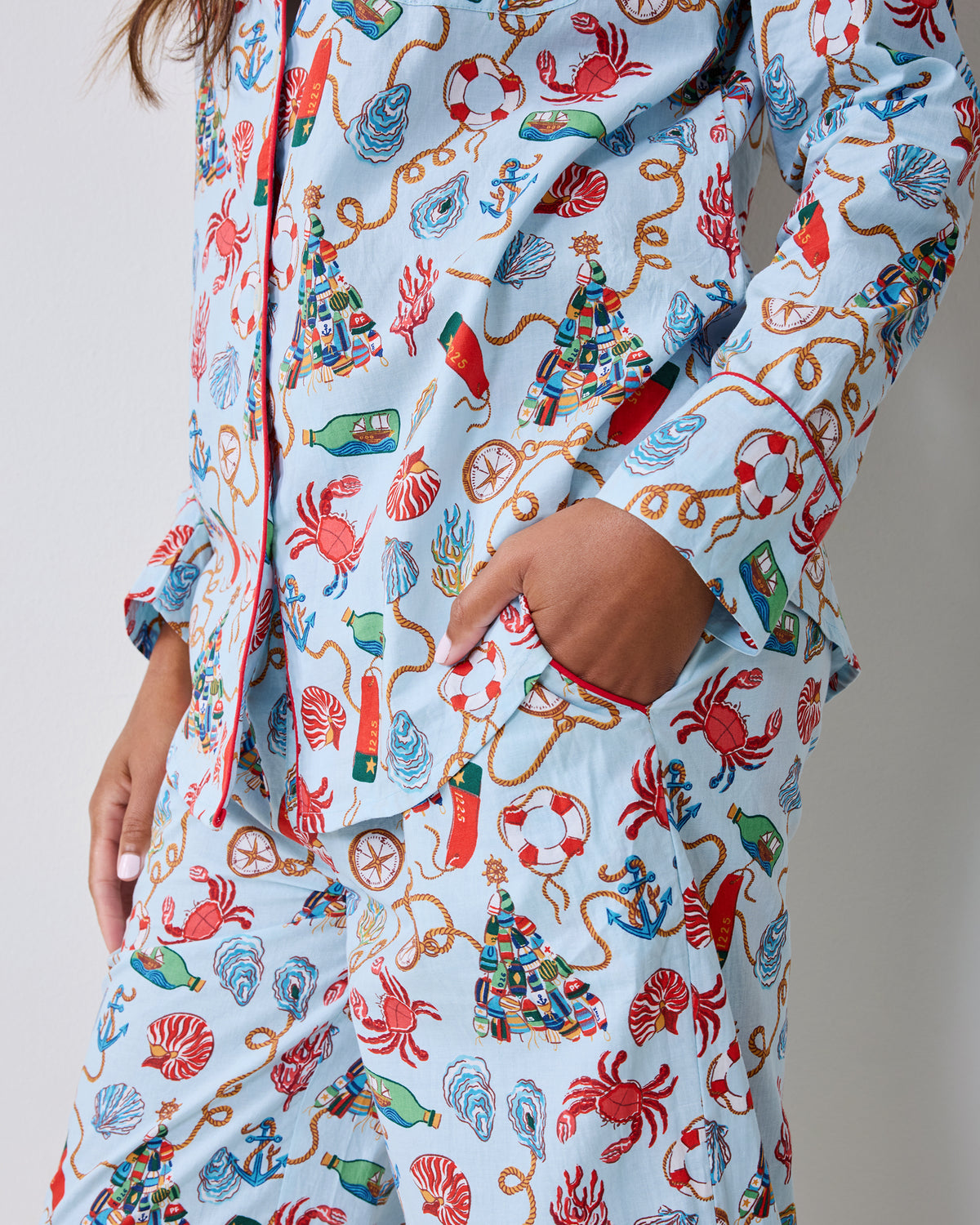 Close-up of a light blue pajama set showing the button-front top, chest pocket, waistband, and nautical Christmas print.