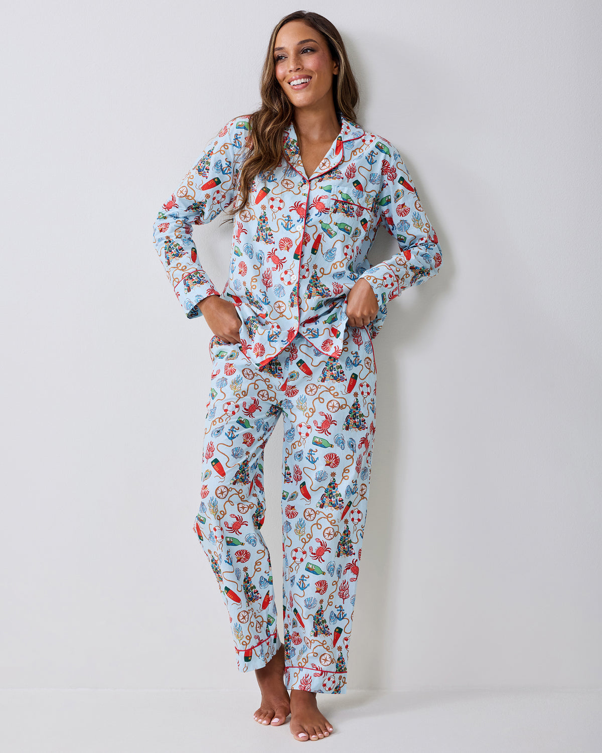 Adult wearing a light blue long-sleeve pajama set with a nautical Christmas print, standing barefoot with hands in the pockets.