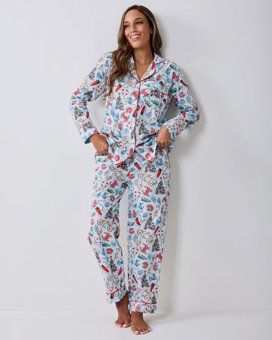 Adult wearing a light blue long-sleeve pajama set with a nautical Christmas print, standing barefoot with hands in the pockets.