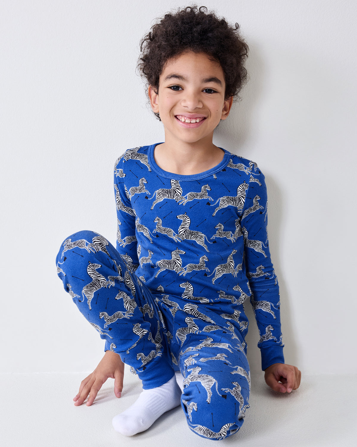 Model seated while wearing the blue long-sleeve pajama set with a zebra-and-arrow print.