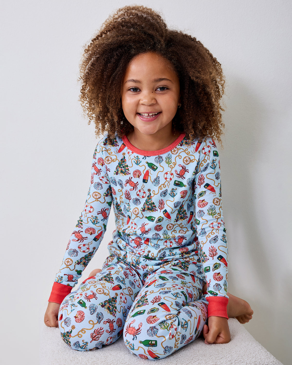 Child seated and wearing a light blue nautical-print long-sleeve pajama set with red cuffs and neckline.
