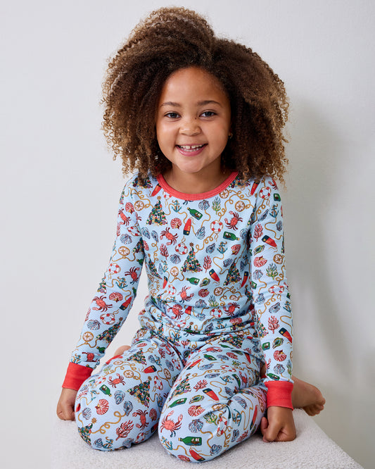 Child seated and wearing a light blue nautical-print long-sleeve pajama set with red cuffs and neckline.