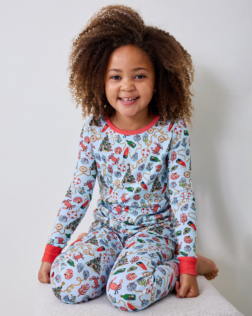 Child seated and wearing a light blue nautical-print long-sleeve pajama set with red cuffs and neckline.