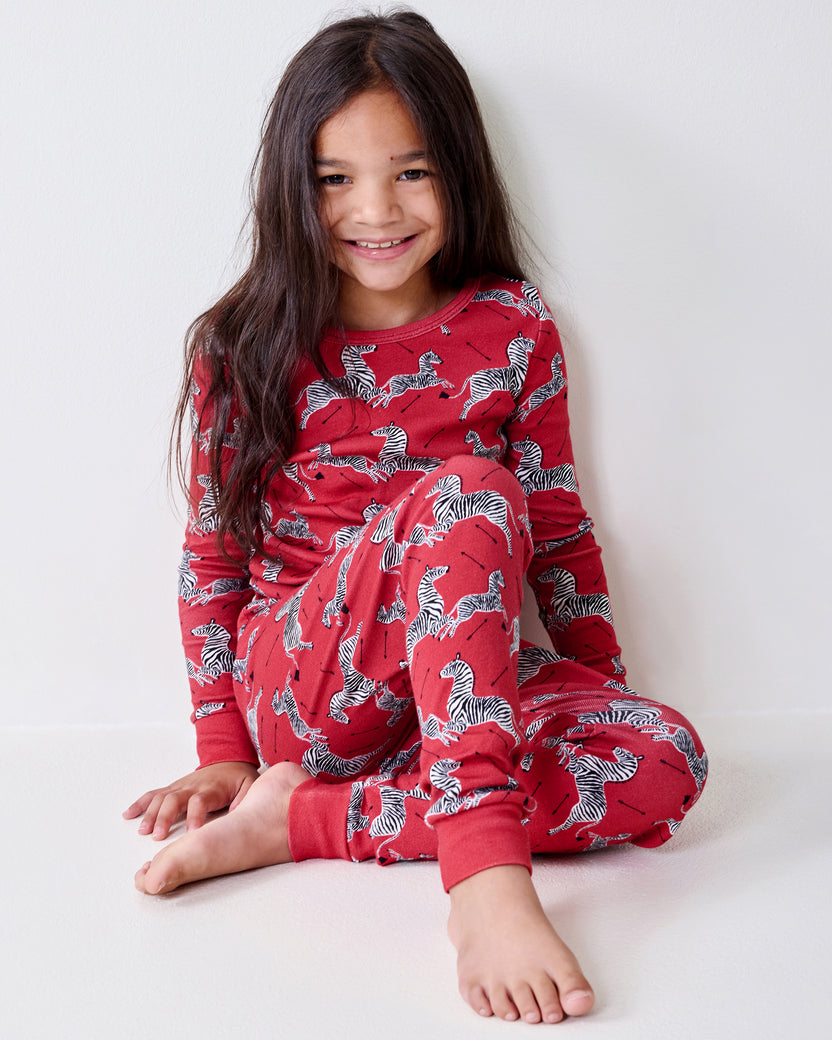 Child seated on the floor wearing a red long-sleeve zebra-print pajama set.