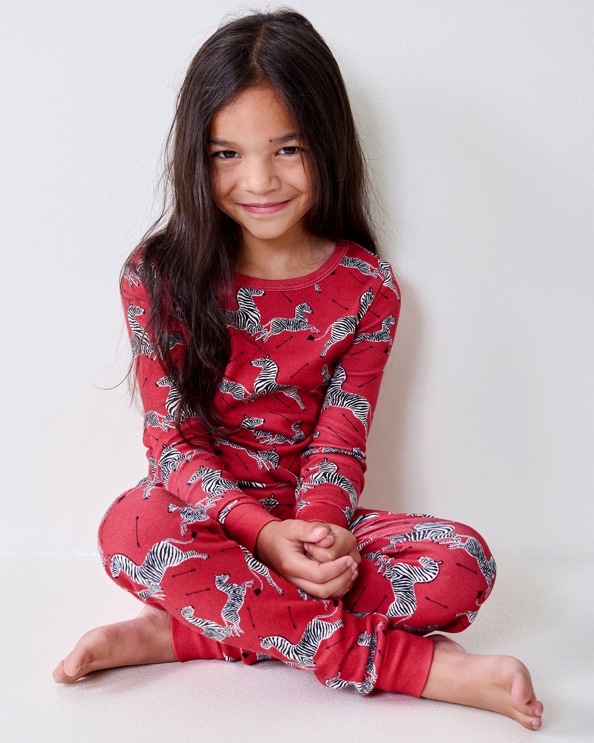 Child seated on the floor wearing a red long-sleeve pajama set with a zebra print.