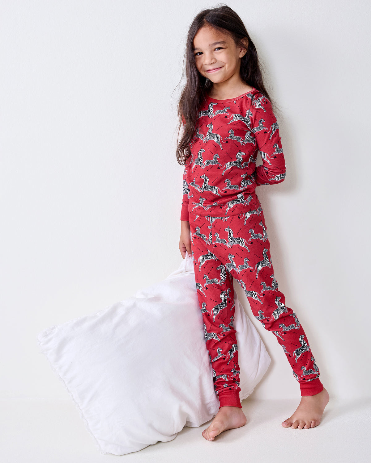Kids' red long-sleeve pajama set with a zebra print, shown on a person standing barefoot beside a white pillow.