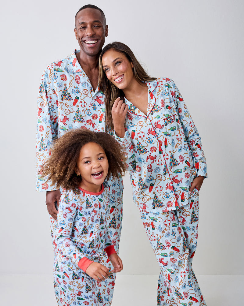 Three people pose in matching light-colored pajamas with a nautical holiday pattern against a plain backdrop.