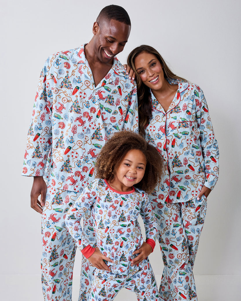Three people wearing matching light blue long-sleeve pajama sets with a nautical Christmas print.