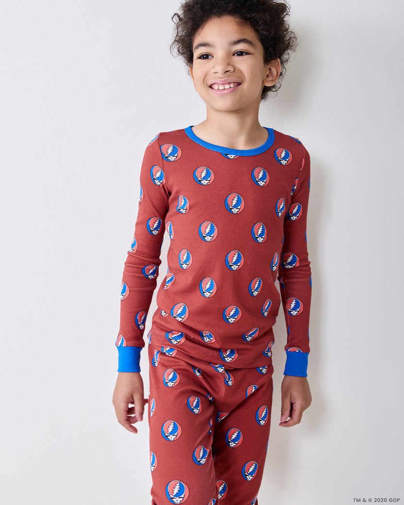 Child wearing a long-sleeve red pajama top and matching pants with repeated circular skull-and-lightning-bolt motifs.