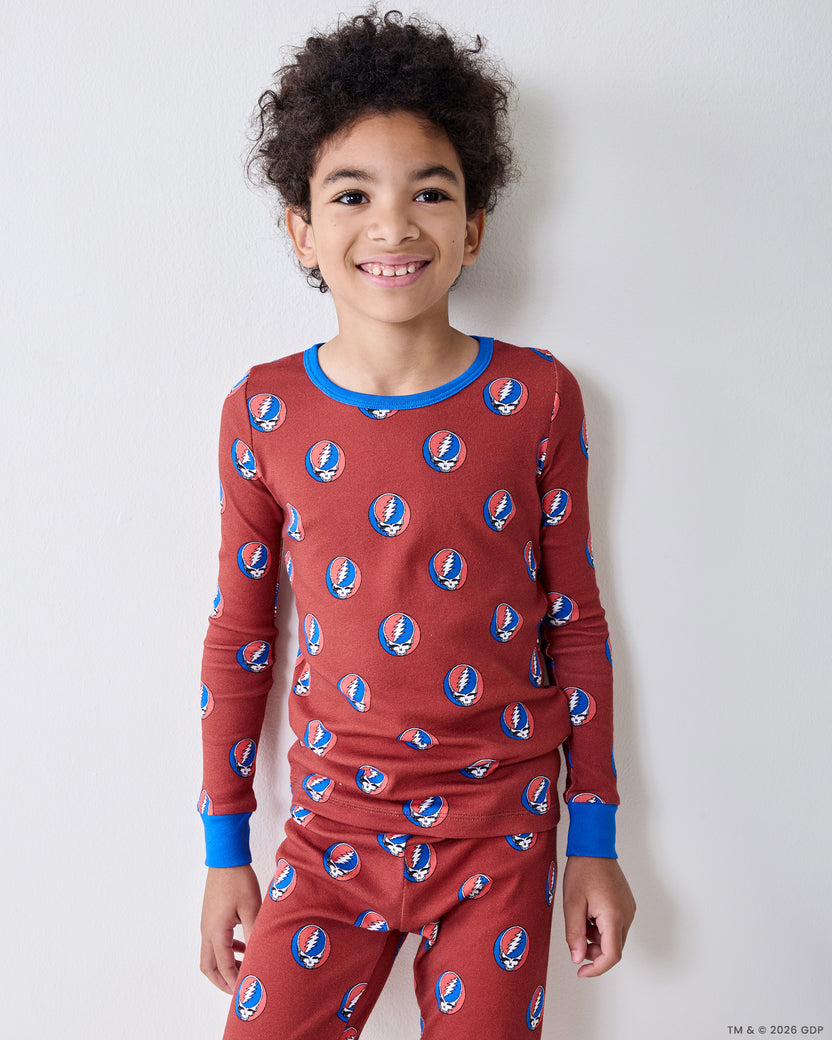 Front view of a child wearing a long-sleeve red pajama top and matching pants with repeated circular skull-and-lightning-bolt motifs.