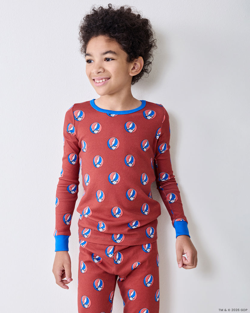 Three-quarter view of a child wearing a long-sleeve red pajama top and matching pants with repeated circular skull-and-lightning-bolt motifs.