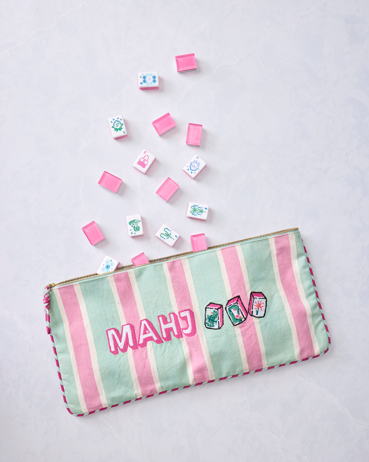 Pale jade striped zippered Mah Jongg tile bag with scattered pink-and-white game tiles.