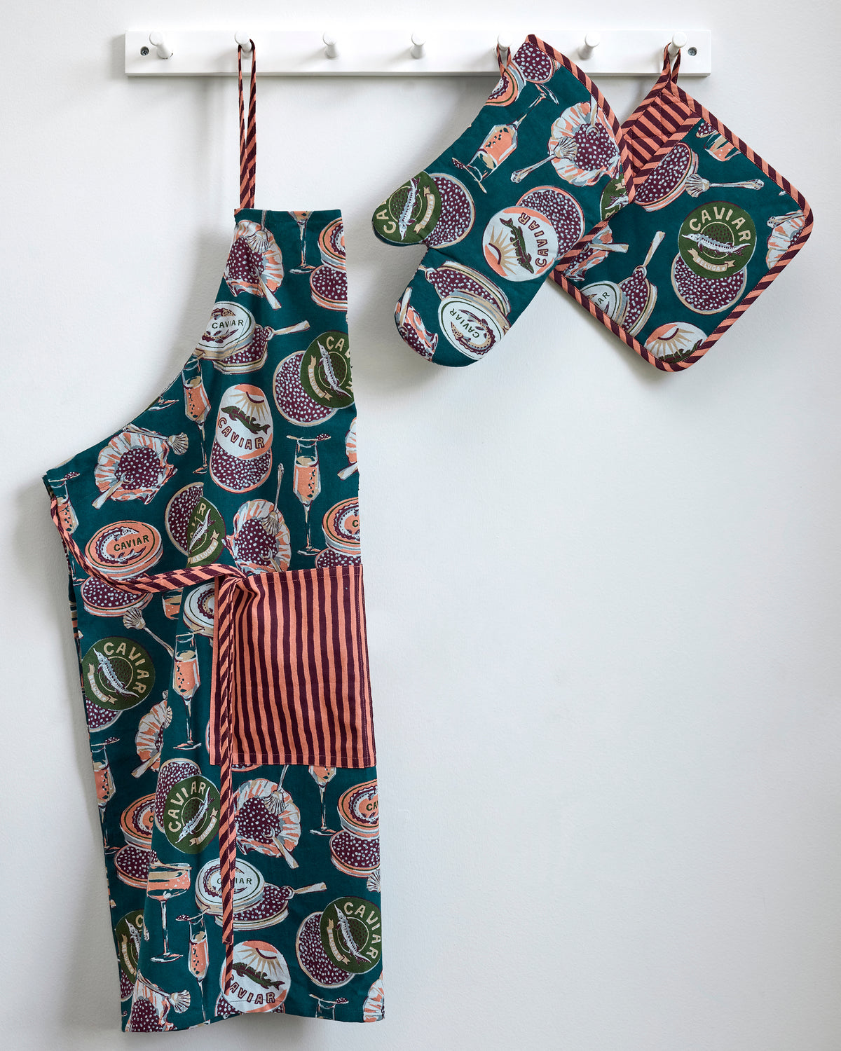 Champagne and caviar print chef’s bundle hanging on hooks with an apron, oven mitt, and pot holder.