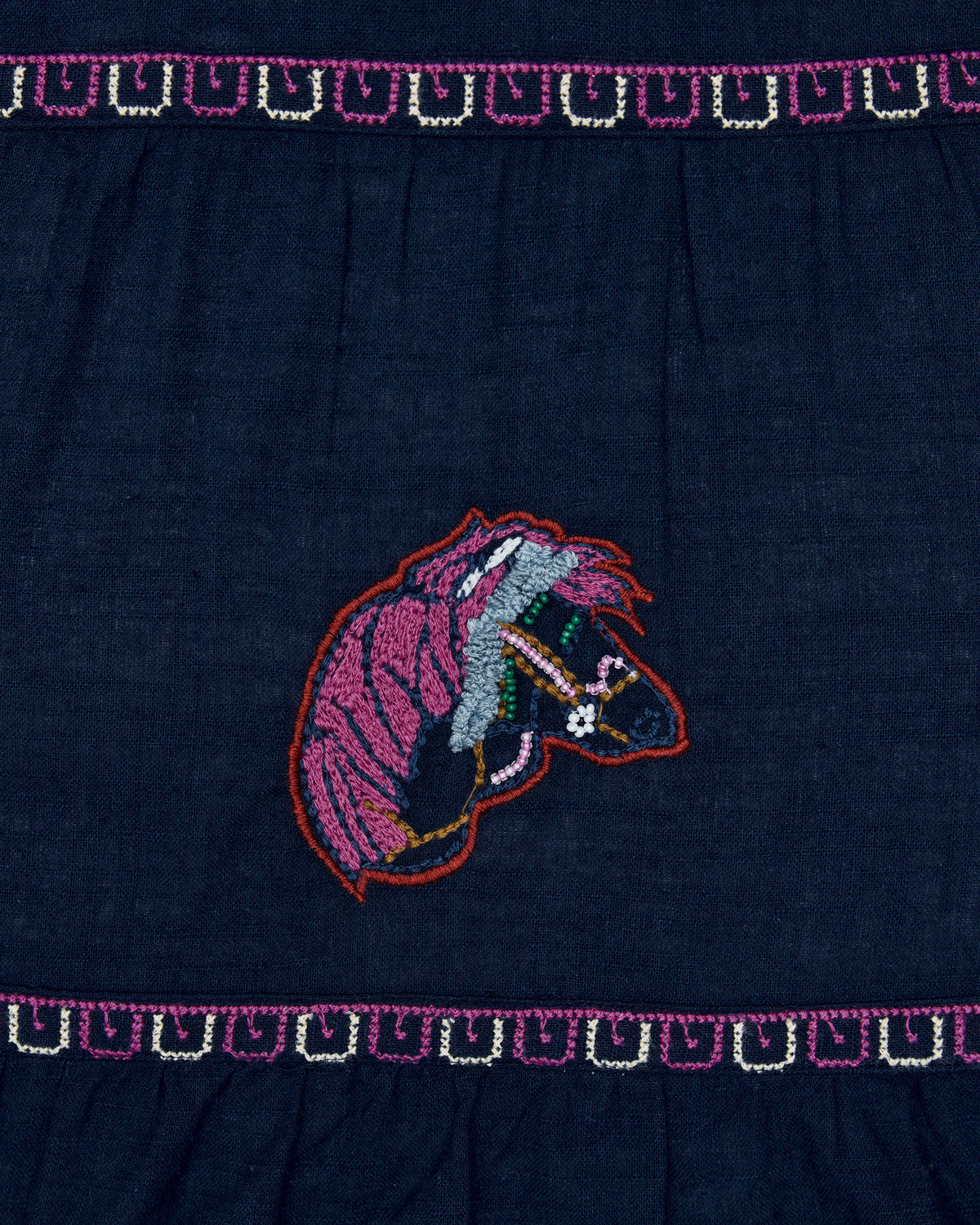 Close view of navy Hallie blouse with colorful embroidered equine head motif and matching stitched borders.