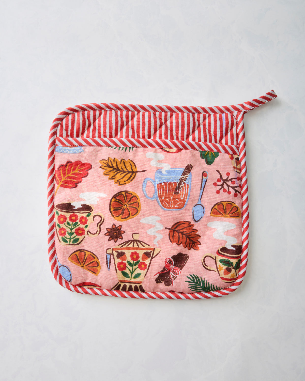 Front of the rose pink quilted pot holder with a tea-themed print and red-and-white striped edging.