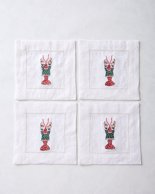 Four white cocktail napkins arranged in a square, each embroidered with a lobster motif.