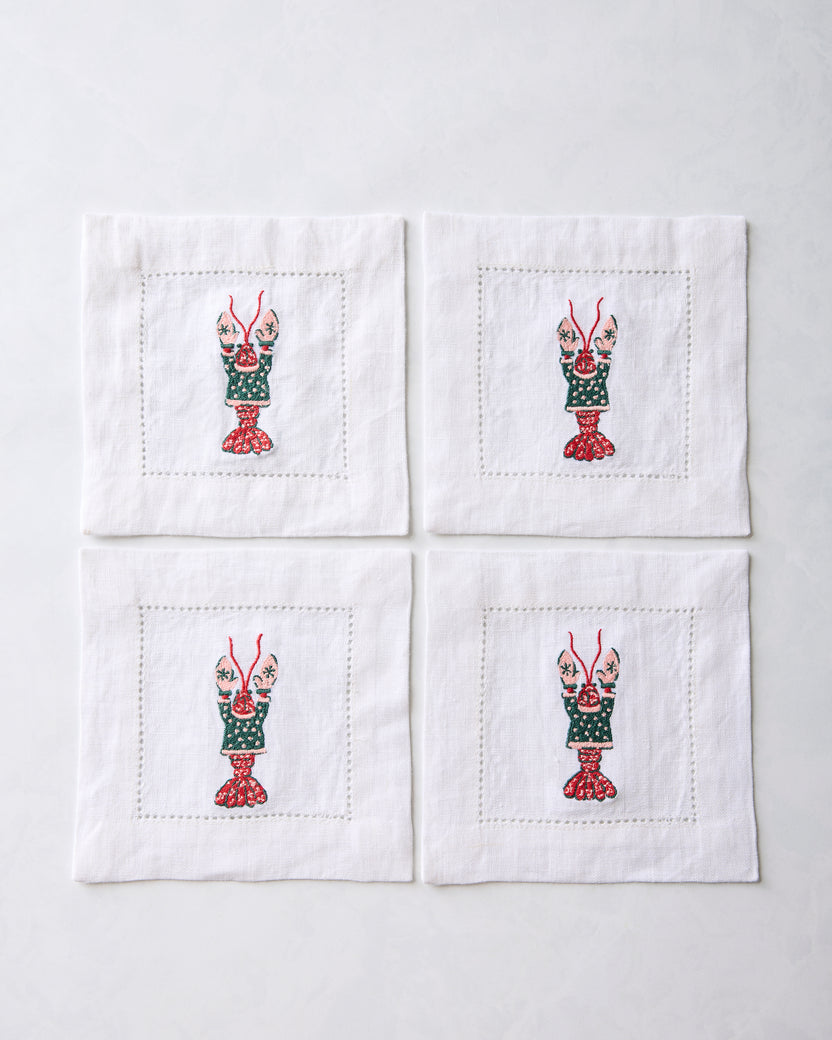 Four white cocktail napkins arranged in a square, each embroidered with a lobster motif.