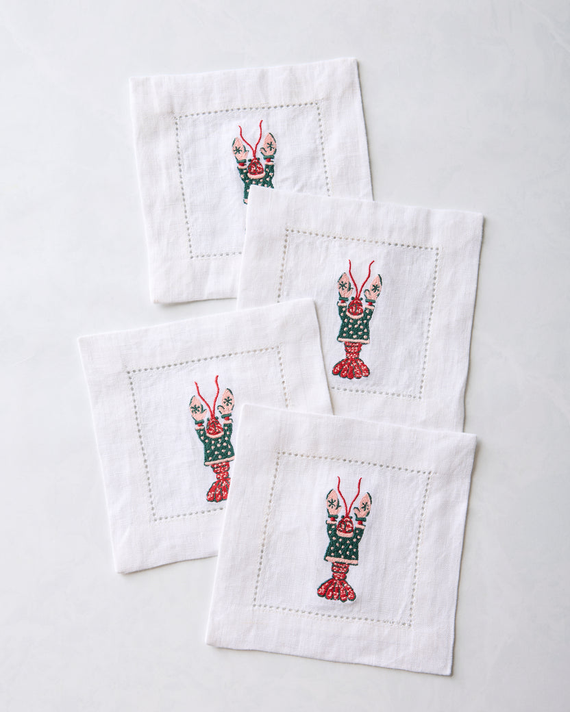 Four white cocktail napkins overlapping in a diagonal arrangement, each with an embroidered lobster motif.