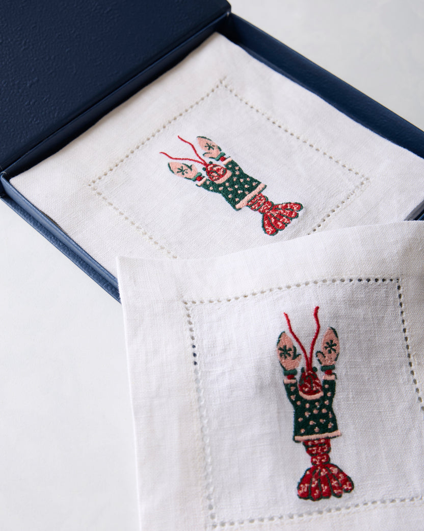 Close view of white embroidered cocktail napkins, with one napkin in a dark blue presentation box and another in the foreground.