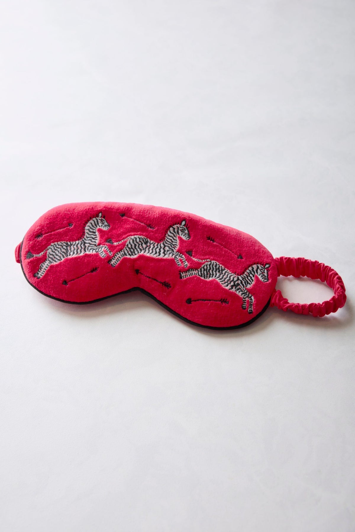 Red embroidered velvet eye mask with zebra motifs and an elastic band, shown flat.