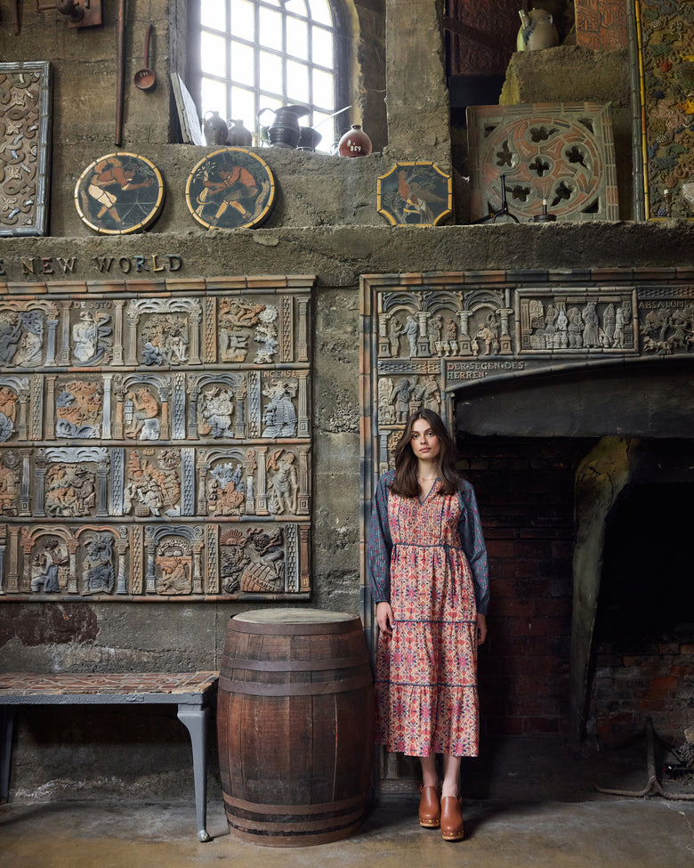 Full-length view of the Winged Tapestry Eden Dress in a patterned floral print, worn in front of an ornate fireplace.