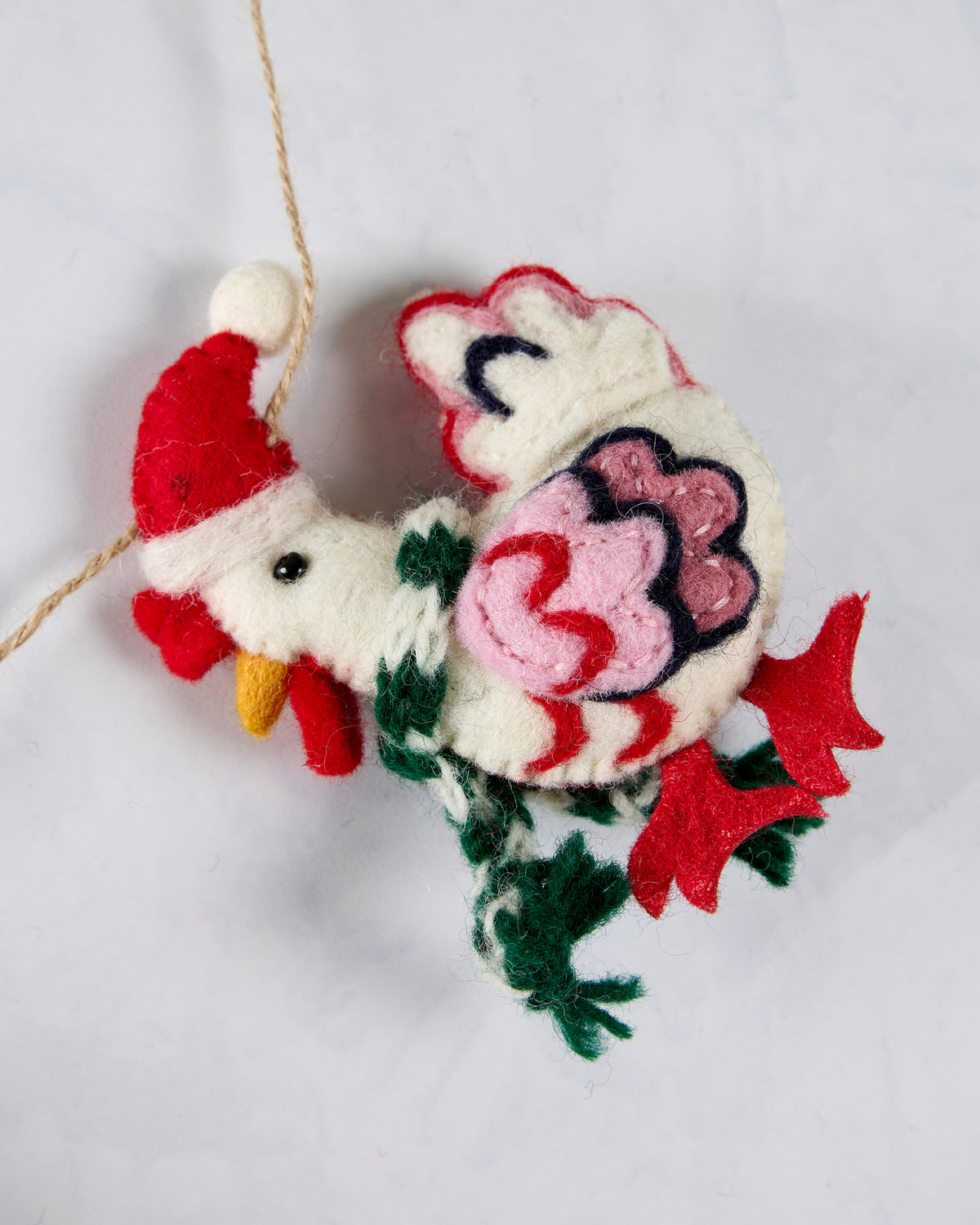 Close-up of a felt hen ornament wearing a Santa hat and scarf, with layered tail feathers and a hanging cord.