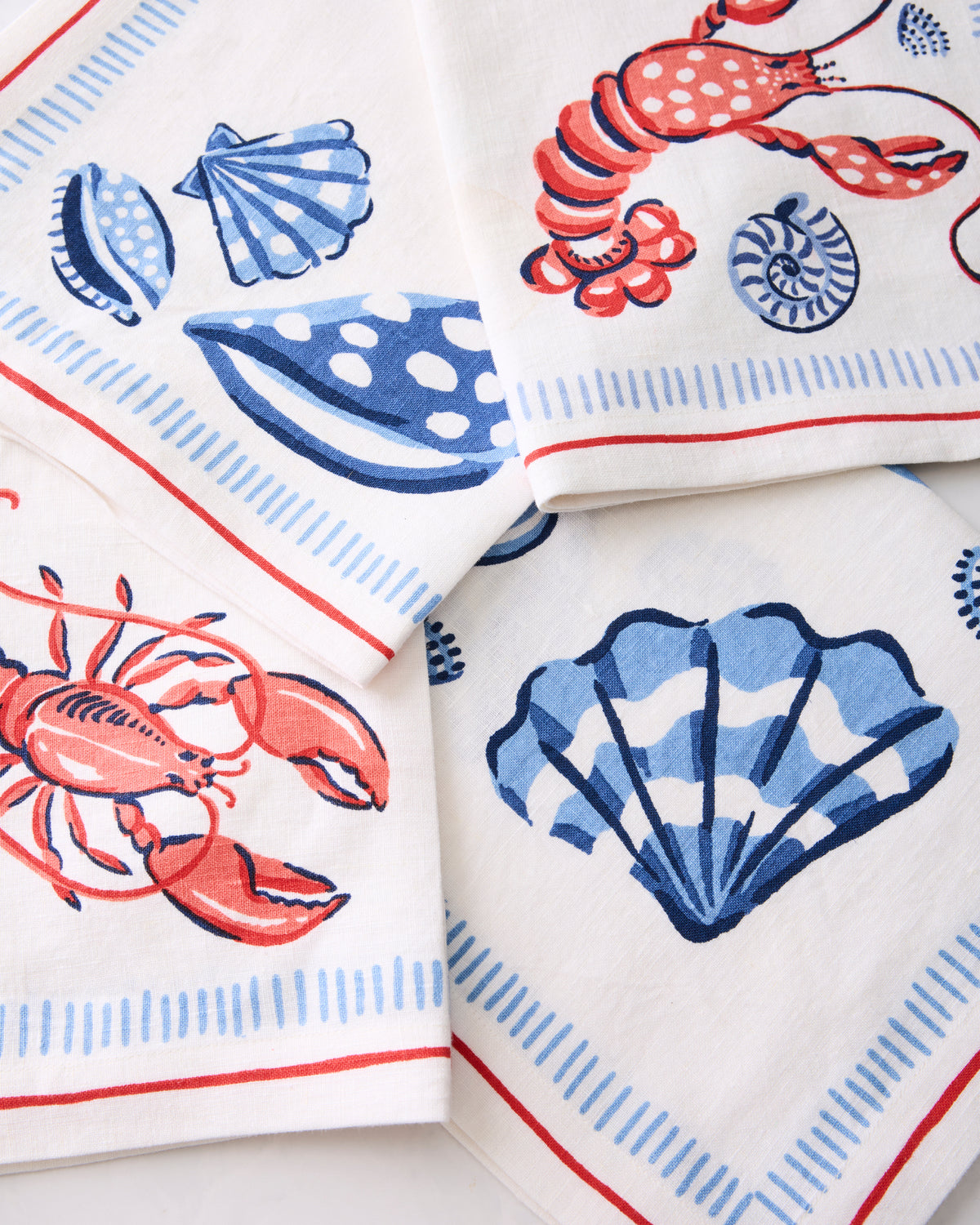 Close-up of four white Lobster Landing napkins showing blue shells and red lobsters.