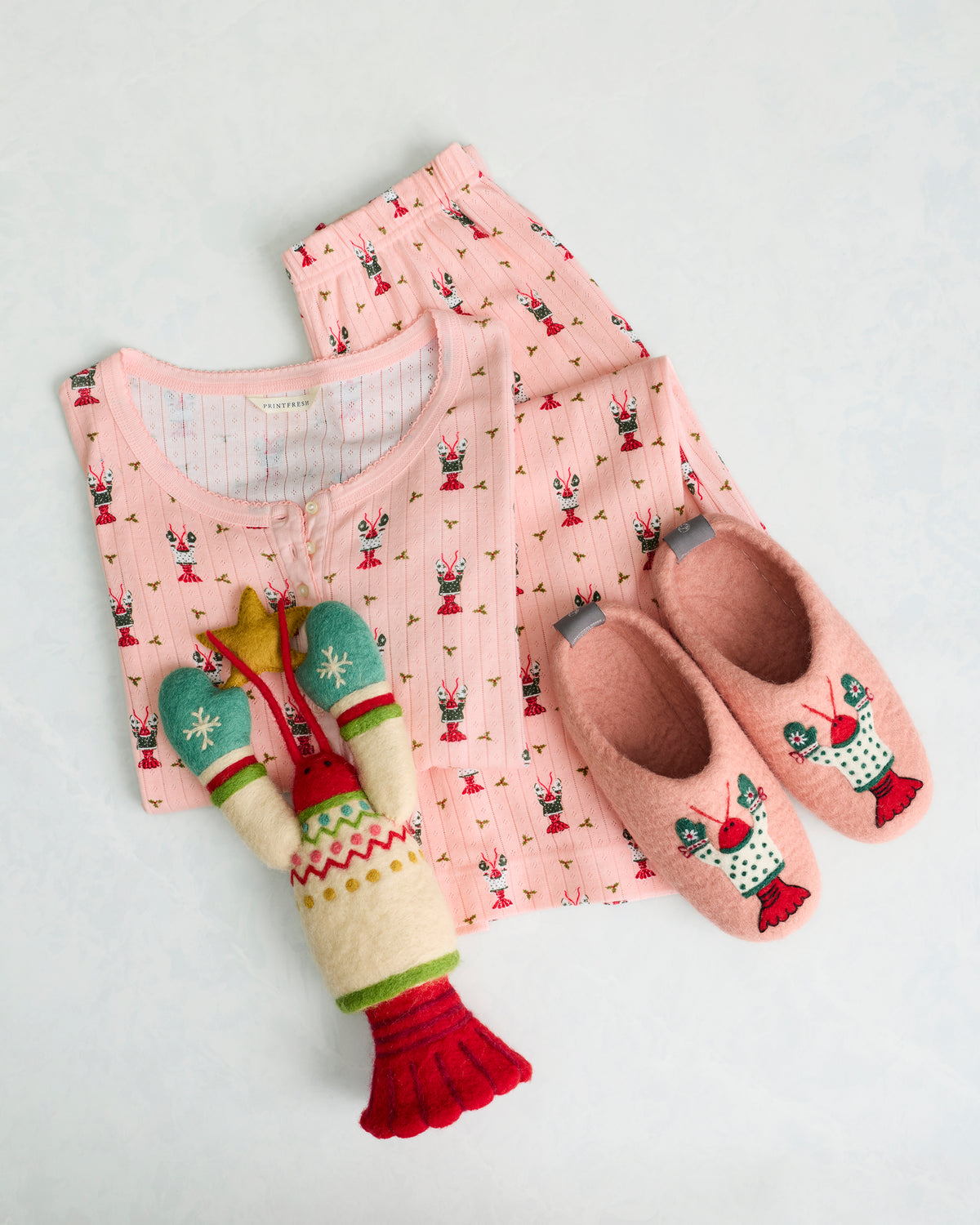Pink Christmas Claws slippers displayed with matching printed pajamas and a felt lobster tree topper.