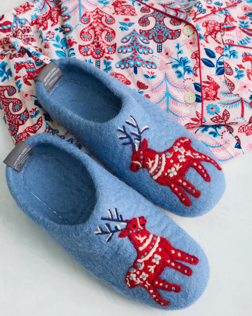 Pair of light blue slippers with red reindeer decorations placed on a patterned pajama top.