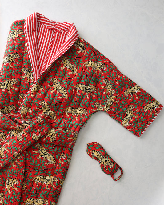 Red quilted robe with a leopard-and-holly print, showing its red-and-white striped lining, alongside a matching eye mask.