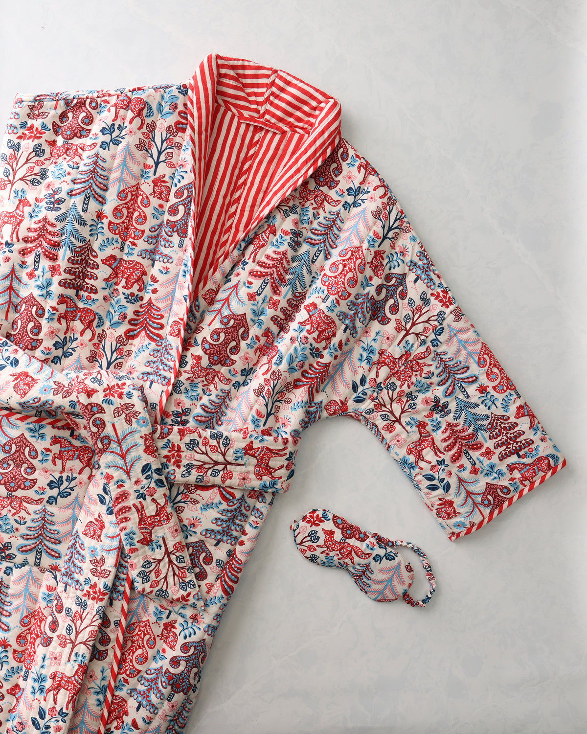 Folklore Forest reversible quilted robe with a matching eye mask, shown with a cream forest print and red-and-white striped lining.